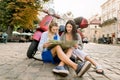 Two friends pretty Caucasian women sitting on the pavement leaning on red scooter and holding city map to find famous