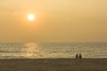 Two friends sit on a sandy beach against the backdrop of the ocean with a sun path and a gray