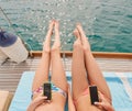 Two friends sunbathing on boat during holiday cruise together using cellphones to send text messages. Two women lying on Royalty Free Stock Photo