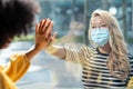 Two friends touching her hands separated by a glass window for social distancing during the corona virus pandemic