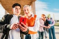 Two friends watching a video in a mobile phone. In the back three friends more browsing with a smartphone.