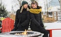 Two friends in winter coats sitting fire in forest