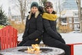 Two friends in winter coats sitting fire in forest