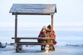 Two frozen women wrapping with red scarf sitting on wooden bench, talking and drinking hot beverages in thermo cups for warm up, Royalty Free Stock Photo