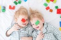 Two funny boys brothers twins lying on white bed in pajamas with colorful constructor