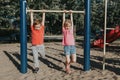 Two funny Caucasian friends hanging on pull-up bars in park on playground. Summer outdoors activity for kids. Active children boy Royalty Free Stock Photo