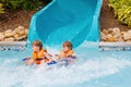 Two funny excited children enjoying summer vacation in water amusement park riding on slide with float. Happy little Royalty Free Stock Photo
