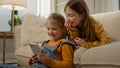 Two funny happy caucasian kids girls sisters friends children having fun playing on phone in living room couch play Royalty Free Stock Photo