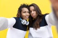 Two funny Hispanic girls taking selfie photo on mobile phone. They are isolated on a yellow background Royalty Free Stock Photo