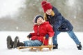 Two funny little girls having fun with a sleigh in beautiful winter park. Cute children playing in a snow.