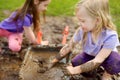 Two funny little girls playing in a large wet mud puddle on sunny summer day. Children getting dirty while digging in muddy soil Royalty Free Stock Photo