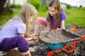 Two funny little girls playing in a large wet mud puddle on sunny summer day. Children getting dirty while digging in muddy soil. Royalty Free Stock Photo