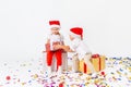 Two funny little kids in Santa hat sitting on gift boxes. Isolated on white background, confetti on a floor. Christmas and new