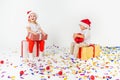Two funny little kids in Santa hat sitting on gift boxes. Isolated on white background, confetti on a floor. Christmas and new Royalty Free Stock Photo