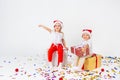 Two funny little kids in Santa hat sitting on gift boxes. Isolated on white background, confetti on a floor. Christmas and new Royalty Free Stock Photo