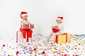 Two funny little kids in Santa hat sitting on gift boxes. Isolated on white background, confetti on a floor. Christmas and new Royalty Free Stock Photo