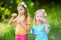 Two funny little sisters blowing soap bubbles outdoors Royalty Free Stock Photo