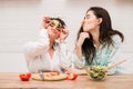 Two girls make funny faces with vegetables in kitchen