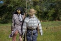 Two funny scarecrows in the field. Pair of scarecrows with hat and stick. Harvest protection and security concept. Rural landscape