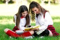 Two funny schoolgirls sit on the grass and read books. Girls, girlfriends, sisters are taught lessons in nature Royalty Free Stock Photo