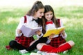 Two funny schoolgirls sit on the grass and read books. Girls, girlfriends, sisters are taught lessons in nature Royalty Free Stock Photo