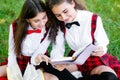 Two funny schoolgirls sit on the grass and read books. Girls, girlfriends, sisters are taught lessons in nature Royalty Free Stock Photo