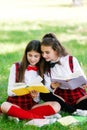 Two funny schoolgirls sit on the grass and read books. Girls, girlfriends, sisters are taught lessons in nature Royalty Free Stock Photo