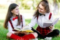 Two funny schoolgirls sit on the grass and read books. Girls, girlfriends, sisters are taught lessons in nature Royalty Free Stock Photo