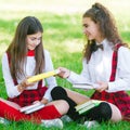 Two funny schoolgirls sit on the grass and read books. Girls, girlfriends, sisters are taught lessons in nature Royalty Free Stock Photo