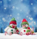 Two funny snowmen and candy cane on the snow. Christmas background