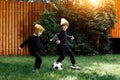 Two funny twin boys play soccer with classic ball on the grass at home.