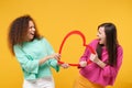 Two funny women friends european and african american girls in pink green clothes posing isolated on yellow wall Royalty Free Stock Photo