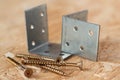 Two galvanized angle brackets and self drilling screws lying on chip board. Blurred background Royalty Free Stock Photo