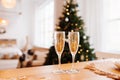 Two gilded glasses for drinks on table, light cozy Scandi room with large Christmas tree and lights on background. selective focus