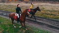 Two ginger horses with equestrians on their back are galloping on the road with puddles Royalty Free Stock Photo