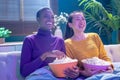 Two girl friends sitting on couch watch a movie and eat popcorn. Funny friends relaxing together. Royalty Free Stock Photo