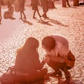 Two girl friends sitting on the pavement and looking on one of their smartphones. Coral color toned photo