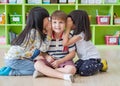 Two girl kids whisper secret at ear of boy in library at kindergarten preschool,Fun and happy children,back to school concept