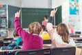 Two girl students raising hands to answer a question in school class