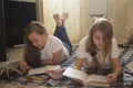 Two girl teens reading a book and drawing while lying on the floor at home