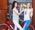 Two girlfriends dressed in fashionable outfits, jeans, tops rest, eat ice cream sitting on a trendy red vintage bicycle. Outdoor. Royalty Free Stock Photo