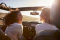 Two girlfriends driving with sunroof open look at each other