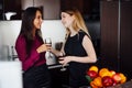 Two girlfriends in elegant clothes relaxing after shopping, drinking wine, laughing and gossiping in the kitchen Royalty Free Stock Photo