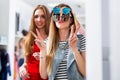 Two girlfriends having fun while doing shopping making faces in the mirror showing V-sign wearing three pair of Royalty Free Stock Photo