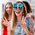 Two girlfriends having fun while doing shopping making faces in the mirror showing V-sign wearing three pair of Royalty Free Stock Photo