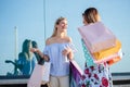 Two girlfriends in front of the shop window, carrying shopping bags. Reflections in glass. Royalty Free Stock Photo