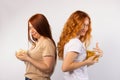 Two girlfriends posing on a white background, hiding bowls with popcorn and potato chips Royalty Free Stock Photo