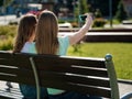 Two girlfriends, young girls sit on a bench and take pictures of selfies.