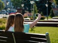 Two girlfriends, young girls sit on a bench and take pictures of selfies. Royalty Free Stock Photo