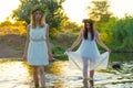 Two girlfriends, young girls in white dresses and flower wreaths on their heads, standing in a river of water, near the shore, Royalty Free Stock Photo